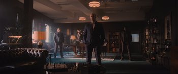 Movie still from “Wrath of Man” (2021), directed by Guy Ritchie – A group of men standing in a room with chess pieces on the floor; Wide shot, Low angle