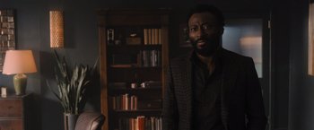 Movie still from “Wrath of Man” (2021), directed by Guy Ritchie – A man standing in front of a bookcase in a room; Medium shot, Over the shoulder angle