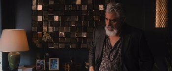 Movie still from “Wrath of Man” (2021), directed by Guy Ritchie – An older man with a gray beard standing in front of a brick wall; Medium shot, Over the shoulder angle