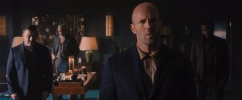 Movie still from “Wrath of Man” (2021), directed by Guy Ritchie – A bald man in a suit stares into the camera; Medium shot, Over the shoulder angle