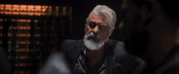Movie still from “Wrath of Man” (2021), directed by Guy Ritchie – An older man with white hair and a gray beard; Close Up shot, Over the shoulder angle