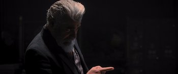 Movie still from “Wrath of Man” (2021), directed by Guy Ritchie – An old man with a white beard is holding his hand out; Close Up shot, Over the shoulder angle