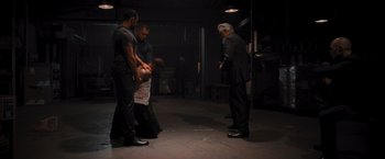 Movie still from “Wrath of Man” (2021), directed by Guy Ritchie – A group of men standing around a man in a black suit; Wide shot, Over the shoulder angle