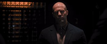 Movie still from “Wrath of Man” (2021), directed by Guy Ritchie – A bald man in a black suit is looking at the camera; Close Up shot, Low angle