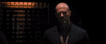 Movie still from “Wrath of Man” (2021), directed by Guy Ritchie – A bald man in a black jacket and a brown tie; Close Up shot, Low angle