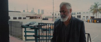 Movie still from “Wrath of Man” (2021), directed by Guy Ritchie – An older man with a gray beard is standing on a park bench; Medium shot, Over the shoulder angle