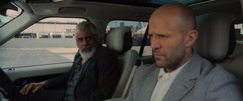 Movie still from “Wrath of Man” (2021), directed by Guy Ritchie – Two men sitting in the back seat of a car; Close Up shot, Over the shoulder angle