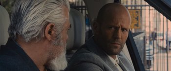 Movie still from “Wrath of Man” (2021), directed by Guy Ritchie – A man with a beard sitting next to a man in a suit; Close Up shot, Over the shoulder angle