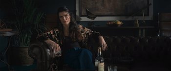 Movie still from “Wrath of Man” (2021), directed by Guy Ritchie – A woman sitting on a couch holding a glass of wine; Medium shot, High angle