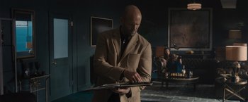 Movie still from “Wrath of Man” (2021), directed by Guy Ritchie – A bald man in a brown suit is looking at a tablet; Medium shot, Over the shoulder angle