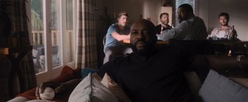 Movie still from “Wrath of Man” (2021), directed by Guy Ritchie – A man sitting on top of a couch next to another man; Medium shot, Low angle