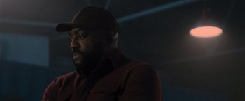 Movie still from “Wrath of Man” (2021), directed by Guy Ritchie – A man with a beard wearing a red jacket and a hat; Close Up shot, Low angle