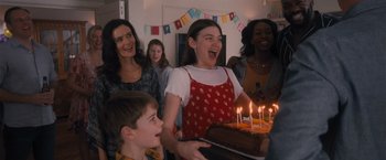 Movie still from “Wrath of Man” (2021), directed by Guy Ritchie – A group of people standing in front of a birthday cake; Medium shot, Over the shoulder angle