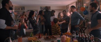 Movie still from “Wrath of Man” (2021), directed by Guy Ritchie – A group of people standing around a table with food on it; Wide shot, High angle
