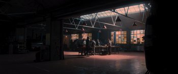 Movie still from “Wrath of Man” (2021), directed by Guy Ritchie – A group of people sitting around a table in a room; Extreme Wide shot, Low angle