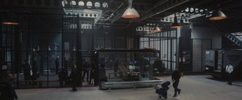 Movie still from “Wrath of Man” (2021), directed by Guy Ritchie – People are standing around inside a building with a glass window; Wide shot, High angle