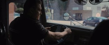 Movie still from “Wrath of Man” (2021), directed by Guy Ritchie – A man driving a truck in the street; Medium shot, Low angle