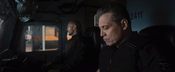 Movie still from “Wrath of Man” (2021), directed by Guy Ritchie – A man sitting next to another man in a vehicle; Close Up shot, Low angle