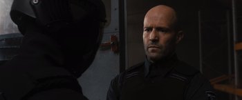 Movie still from “Wrath of Man” (2021), directed by Guy Ritchie – A bald man in a black shirt and a helmet; Close Up shot, Over the shoulder angle