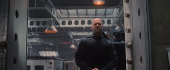 Movie still from “Wrath of Man” (2021), directed by Guy Ritchie – A man in a black jacket standing in a room; Medium shot, Low angle