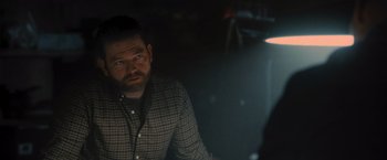 Movie still from “Wrath of Man” (2021), directed by Guy Ritchie – A man sitting in a dark room with a light shining on him; Close Up shot, Over the shoulder angle