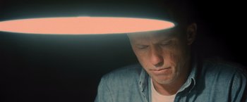 Movie still from “Wrath of Man” (2021), directed by Guy Ritchie – A person under a light fixture; Close Up shot, Overhead angle