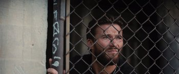 Movie still from “Wrath of Man” (2021), directed by Guy Ritchie – A person behind a chain link fence; Close Up shot, Low angle