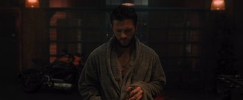 Movie still from “Wrath of Man” (2021), directed by Guy Ritchie – A man in a robe looking at his watch; Medium shot, Low angle