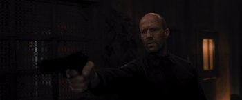 Movie still from “Wrath of Man” (2021), directed by Guy Ritchie – A man holding a gun while wearing a black shirt; Close Up shot, Low angle