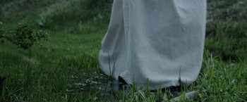 Movie still from “Wuthering Heights” (2022), directed by Bryan Ferriter – A person walking in the grass near a body of water; Extreme Close Up shot, Low angle