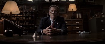 Movie still from “X-Men: First Class” (2011), directed by Matthew Vaughn – A man sitting at a table in front of a lamp; Medium shot, Low angle