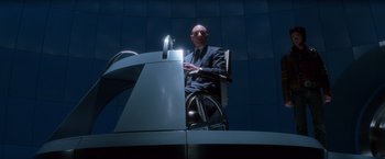 Movie still from “X-Men” (2000), directed by Bryan Singer – A man sitting in a chair in front of a microphone; Wide shot, Low angle