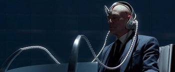 Movie still from “X-Men” (2000), directed by Bryan Singer – A bald man wearing a suit and tie with headphones around his neck; Close Up shot, Over the shoulder angle