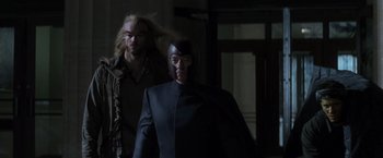 Movie still from “X-Men” (2000), directed by Bryan Singer – Two people in a dark room , one of whom is wearing a helmet and the other is wearing a suit; Medium shot, Low angle