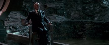 Movie still from “X-Men” (2000), directed by Bryan Singer – A man in a suit and tie sitting on a chair; Medium shot, Low angle