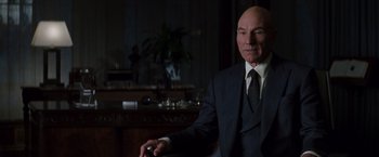Movie still from “X-Men” (2000), directed by Bryan Singer – A man in a suit and tie sitting in front of a table; Medium shot, Over the shoulder angle