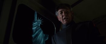 Movie still from “X-Men” (2000), directed by Bryan Singer – An older man in a black suit standing in front of the statue of liberty; Medium shot, Low angle