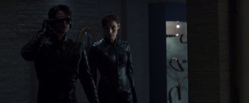 Movie still from “X-Men” (2000), directed by Bryan Singer – A woman in a black leather jacket standing next to a wall; Medium shot, Over the shoulder angle