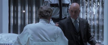 Movie still from “X-Men” (2000), directed by Bryan Singer – A man in a suit and tie standing next to another man in a suit and tie; Close Up shot, Over the shoulder angle