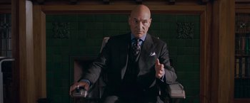 Movie still from “X-Men: The Last Stand” (2006), directed by Brett Ratner – A man in a suit and tie sitting in a chair; Medium shot, Low angle