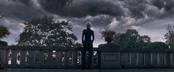 Movie still from “X-Men: The Last Stand” (2006), directed by Brett Ratner – A woman standing on a balcony under a cloudy sky; Wide shot, Low angle