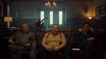 Movie still from “Fargo” (2014), created by Noah Hawley – A man sitting on a couch next to another man in a room; Wide shot, Low angle