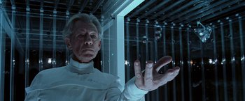 An older man in a white suit is holding his hand out