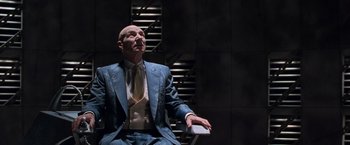 Movie still from “X2” (2003), directed by Bryan Singer – A bald man in a suit and tie holding a white object; Medium shot, Low angle