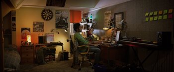 Movie still from “Yesterday” (2019), directed by Danny Boyle – A man sitting at a desk in a room with posters on the wall; Wide shot, High angle