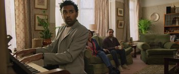 Movie still from “Yesterday” (2019), directed by Danny Boyle – Three people sitting on a couch in a living room; Medium shot, Over the shoulder angle