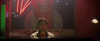 Movie still from “Yesterday” (2019), directed by Danny Boyle – A man standing in front of a poster of a person; Medium shot, Low angle