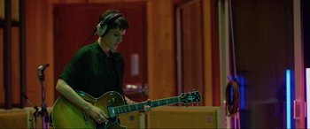 Movie still from “Yesterday” (2019), directed by Danny Boyle – A man with headphones on playing an electric guitar; Medium shot, High angle