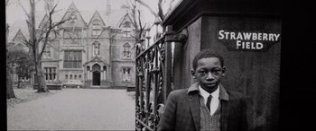 Movie still from “Yesterday” (2019), directed by Danny Boyle – A black and white photo of a young man in front of a building; Medium shot, Low angle