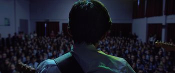 Movie still from “Yesterday” (2019), directed by Danny Boyle – A man is standing in front of an audience; Medium shot, Over the shoulder angle